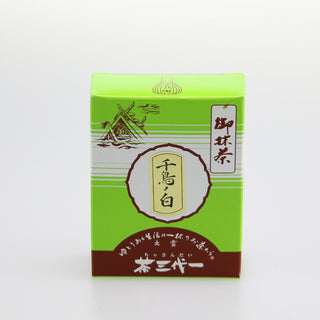 Eine grüne Packung Matcha mit der Aufschrift "Chidori no Shiro". Links oben auf der Packung befindet sich eine Zeichnung, die einen alten japanischen Schrein darstellt. Die Packung hat zudem japanische Schriftzeichen und eine braunrote Basis. Der Hintergrund ist weiß und neutral gehalten.