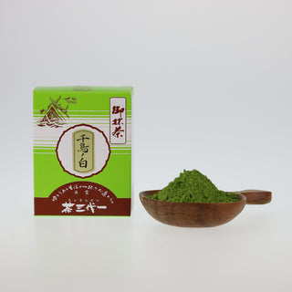 Verpackung von Shinkoko Matcha Chidori no Shiro in einer grünen Schachtel, daneben eine Holzschale mit grünem Matcha-Pulver.