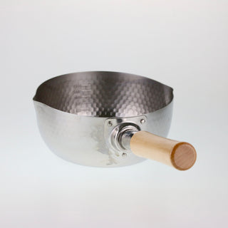 Schräge Aufsicht auf einen Edelstahltopf mit gehämmerter Struktur, bei der der helle Holzgriff und die metallene Griffbefestigung im Vordergrund stehen.