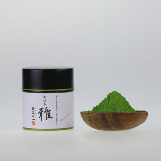 matcha Miyabi in schwarzer Dose mit Kalligraphie, daneben Matcha-Pulver in Holzteller