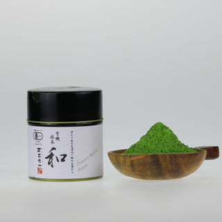 matcha nagomi in schwarzer Dose mit Kalligraphie, daneben Matcha-Pulver in Holzteller