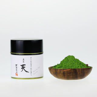 matcha Ten in schwarzer Dose mit Kalligraphie, daneben Matcha-Pulver in Holzteller