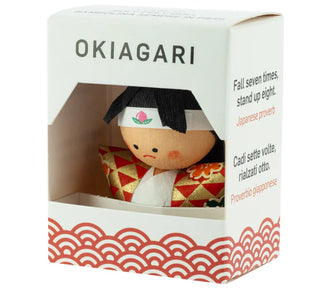 Okiagari-Figur "Der Tapfere Momotaro" in dekorativer Verpackung mit Sichtfenster und der Aufschrift „Fall seven times, stand up eight – Japanese proverb“.