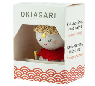 Okiagari „Jizō“ in dekorativer Verpackung mit Sichtfenster, Aufschrift „Fall seven times, stand up eight“.