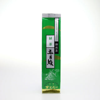 Eine längliche Packung "Satsuki Midori Sencha". Sie ist hellgrün. Am unteren Rand ist eine Zeichnung in weiß, auf der ein alter japanischer Schrein abgebildet ist. Zwei senkrechte Streifen in Weiß, Silber und Schwarz, versehen mit japanischen Schriftzeichen, sind ebenfalls auf der Vorderseite zu sehen. 