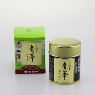 Links ist die grüne Verpackung des Matcha "Seihou" mit japanischen Schriftzeichen und einer Zeichnung eines japanischen Schreins zu sehen. Rechts daneben steht die dazugehörige Matcha-Dose mit goldenem Deckel und schwarzem Etikett. Der Hintergrund ist weiß und schlicht gehalten.