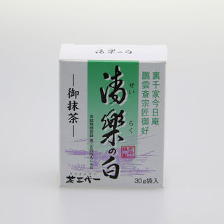 Eine weiße Packung Matcha mit der Bezeichnung "Seiraku no Shiro". Die Verpackung hat einen grünen Streifen und ist mit japanischen Schriftzeichen versehen. Der Hintergrund ist neutral und weiß gehalten.