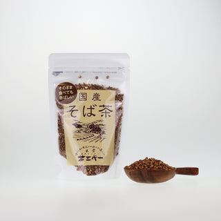 Sobacha Buchweizentee in durchsichtiger Verpackung mit japanischen Schriftzeichen, daneben ein Holzteller mit gerösteten Buchweizenkörnern.